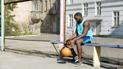 Triste-hombre-afroamericano-sentado-en-el-banquillo-y-jugando-a-la-pelota,-soledad