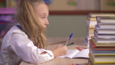 Muchacha-de-la-escuela-escribiendo-en-un-cuaderno-de-escuela-y-mostrando-pulgar-hacia-arriba