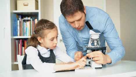 Kleines-Mädchen-mit-Lehrer-im-naturwissenschaftlichen-Unterricht-mit-Mikroskop-auf-dem-Tisch.