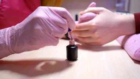 the-manicure-master-paints-the-client-nails-with-nail-polish.-beauty-saloon.-soft-focus.-Basque-with-nail-varnish-close-up.-4-k