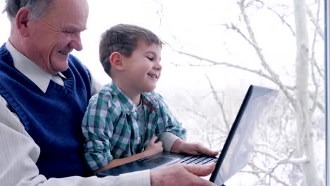 laughing-boy-with-grandfather-with-laptop-sitting-together-at-home