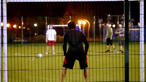 In-the-foreground-is-the-goalkeeper,-another-young-man-kicks-the-ball-and-hits-the-goal,-night-shooting