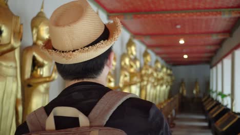 Jóvenes-asiáticos-viajan-a-turistas-de-mochila-caminar-dentro-en-Wat-Pho-templo-con-estatuas-de-Buda-dorado-en-la-fila-en-Bangkok,-Tailandia---viajes-mochila-explorar-ciudad-en-Asia