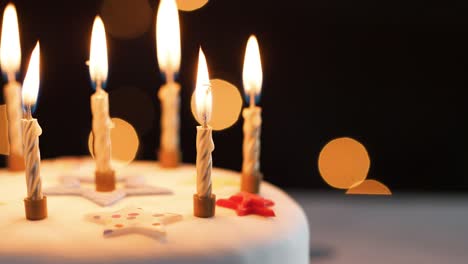 Close-up-of-lit-candles-on-a-white,-decorated-birthday-cake,-bokeh-lights-in-the-background