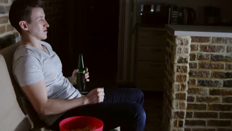 Young-man-watching-TV-with-beer-and-chips