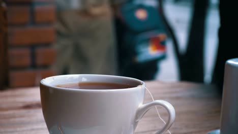 Blanco-taza-de-té-caliente-sobre-la-mesa-en-un-café-en-el-fondo-de-la-ventana-de-la-calle