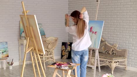 A-happy-girl-artist-spinning-around-herself-in-a-studio-among-many-paintings.