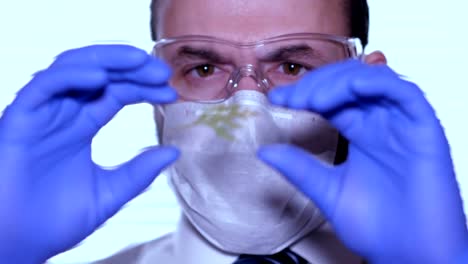 Biologist-examines-sample.-Science,-biology,-ecology.-Professional-scientist-wearing-protective-mask-working-with-herb-samples-in-his-laboratory.-Male-scientist-looking-at-plant-leaf-in-glass-slide.