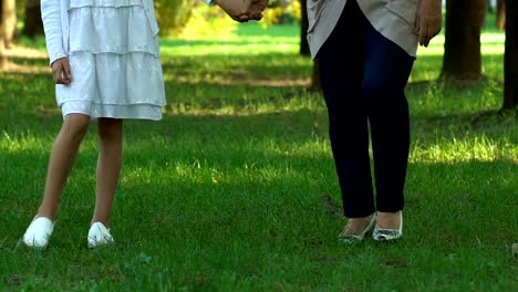 Woman-holding-little-girl-hand-and-walking-in-green-park-at-summer,-weekend