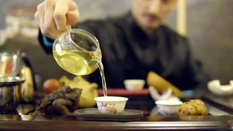 Master-man-pours-green-tea-from-a-glass-teapot-into-a-white-mug