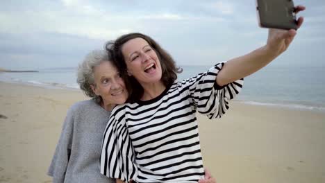 Erwachsene-Tochter-umarmt-und-senior-Mama-Selfie-mitnehmen