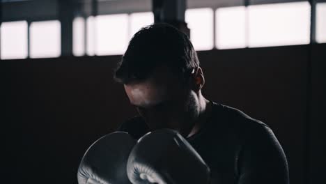 Ajuste-el-boxeador-entrenando-en-un-saco-de-boxeo-en-un-estudio-de-boxeo-interior