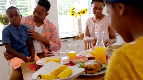 Vista-frontal-de-la-familia-black-feliz-comiendo-en-mesa-de-comedor-en-una-casa-confortable-4k