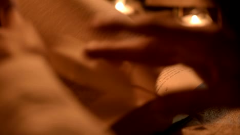 Big-Close-up-girl-magician-in-a-dark-room-with-candlelight-looking-for-a-spell-in-a-book.-Low-key-live-camera.