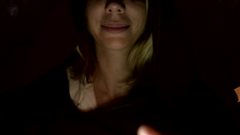 Close-up-bottom-of-the-face-of-the-girl-magician-in-a-dark-room-with-candlelight-smiling-from-the-flash-below.-Low-key-live-camera