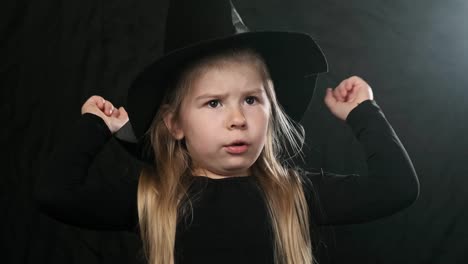 Halloween-witch-in-black-dress-and-hat-conjures.-Close-up-of-little-blonde-girl