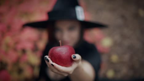 Mujer-como-bruja-de-negro-ofrece-manzana-roja-como-símbolo-de-tentación,-veneno.-Concepto-de-cuento-de-hadas,-Halloween,-cosplay.