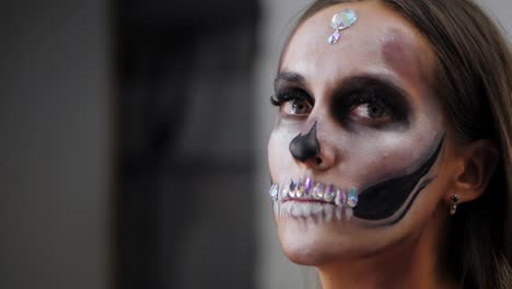 Unheimlich-junges-Mädchen-mit-kreative-Halloween-Gesicht-Kunst-in-der-Umkleidekabine.-Porträt-des-glamourösen-Totenkopf-mit-Strass-und-Pailletten.-Professionelle-Schminke-für-die-Feier