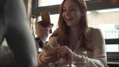 Frau-im-Restaurant-reagiert-auf-ein-lustiges-Foto-auf-Handy-Bildschirm