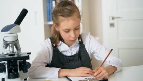 Little-girl-in-science-class-with-microscope-on-the-table.