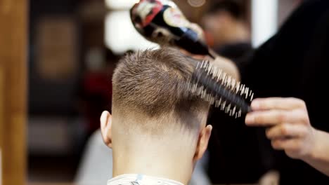 Hairdresser-dries-and-combs-hair-of-young-man