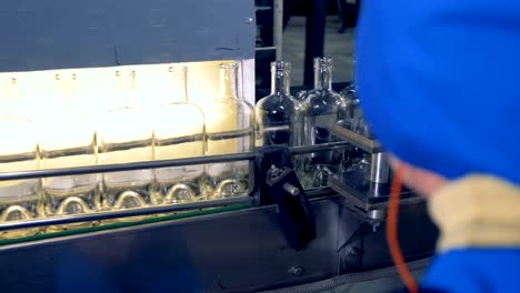 Empty-bottles-go-on-a-line,-while-a-factory-worker-watches-the-technology.-4K.