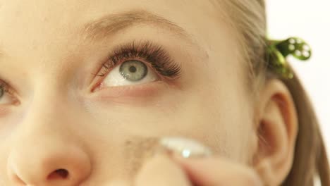 Close-up-portrait-young-woman-during-applying-tone-cream-on-skin-around-eyes-in-makeup-studio.-Professional-makeup-for-woman-on-master-class-in-beauty-school