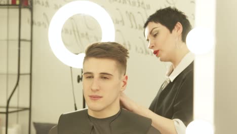 Estilista-mujer-acabado-peinado-después-del-espejo-frontal-de-peluquería-en-estudio-de-belleza.-Cerca-de-haircutter-hacer-peinado-hombre-durante-el-trabajo-con-el-cliente-en-peluquería