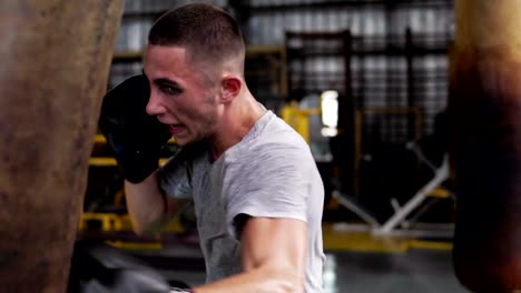 Cerca-de-un-boxeador-macho-pelo-corto,-joven-haciendo-puches-fuerte-en-negro-guantes-de-boxeo.-Trabajando-con-saco-de-boxeo-en-el-estudio-de-boxeo