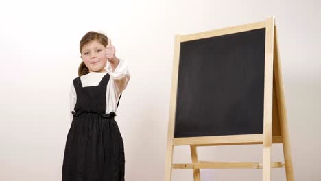 A-happy-girl-dressed-as-a-teacher-in-front-of-a-small-blackboard-holds-her-arms-folded-and-smiles.