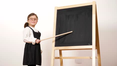 Ein-fröhliches-Mädchen-gekleidet-wie-ein-Lehrer-vor-einer-kleinen-Tafel-hält-den-verschränkten-Armen-und-lächelt.