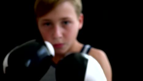 El-niño-participa-en-el-boxeo.-En-primer-plano-las-manos-en-guantes-blanco-y-negro,-cara-de-niño-es-borrosa.-Un-boxeador-en-un-gris-deportes-camisa-se-encuentra-en-un-fondo-oscuro