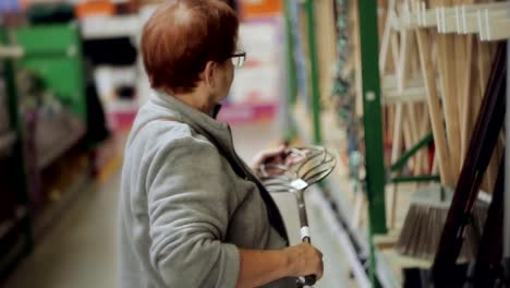 An-elderly-woman-in-a-hypermarket-in-the-Department-tools-chooses-necessary-equipment-for-the-garden