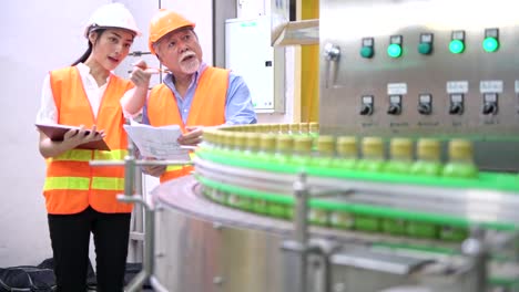 Senior-quality-inspector-teaching-junior-team-member-in-factory.-Chinese-old-male-with-his-young-team-discussing-quality-issue-with-bottle-production-line-in-background.