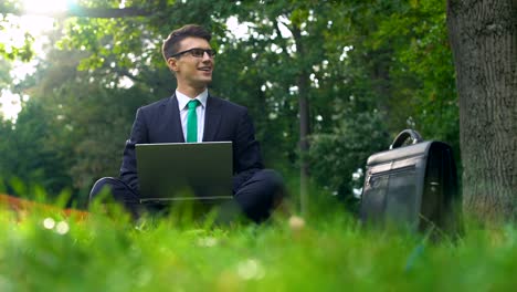 Business-man-sitting-on-grass-and-working-on-laptop-in-park-outside-office