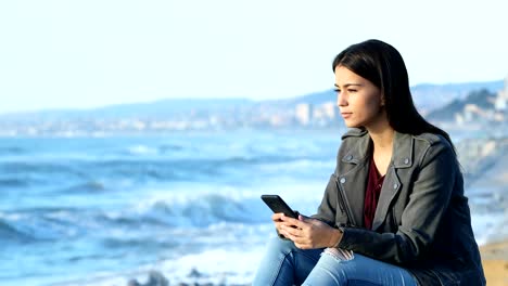 Comprobación-de-teléfono-adolescente-y-mirando-el-horizonte-en-la-playa