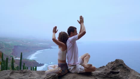 Mann-und-Frau-sitzen-auf-einem-Berg-auf-einem-Felsen-zurück-zu-meditieren-und-Yoga-auf-dem-Hintergrund-des-Ozeans-zu-tun.