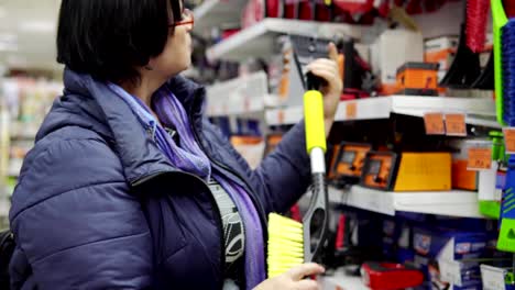 Eine-reife-Frau-wählt-eine-Bürste-mit-Schaber-im-Supermarkt.