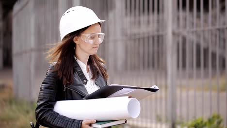 Chica-estudiante-de-casco-protector-y-gafas-e-inspecciona-el-sitio-de-construcción,-utilizando-la-documentación-técnica