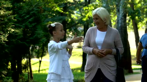 Little-girl-walking-with-granny-and-telling-her-stories-from-school-life,-trust