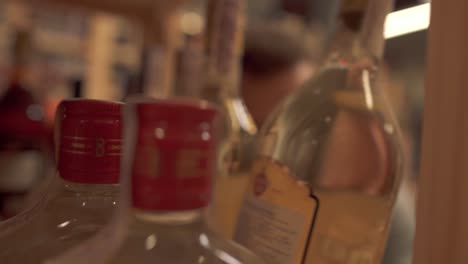 Guy-taking-a-bottle-of-alcoholic-beverage-from-a-wooden-shelf-in-liquor-store.-Man-is-out-of-focus.