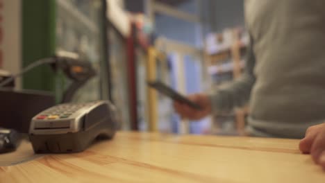 Guy-paying-with-mobile-phone-contactless-payment-at-liquor-store.-Seller-counts-for-a-bottle-of-white-wine.