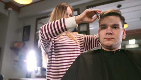 Tiro-interior-del-proceso-de-trabajo-en-peluquería-moderna.-Retrato-de-vista-lateral-de-hombre-joven-atractivo-conseguir-moda-corte-de-pelo.-Cliente-de-servicio-de-peluquería-masculina,-haciendo-corte-de-pelo-con-peine-y-tijeras-de-metal