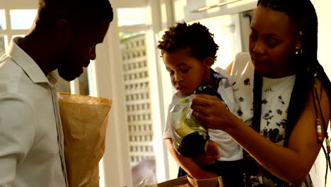 Front-view-of-young-black-mother-and-son-looking-in-grocery-bag-in-kitchen-of-comfortable-home-4k