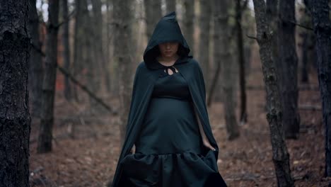 Black-witch-in-hood-walks-in-autumn-scary-forest.Womanl-in-long-dress.-Halloween,-horror,-concept,-cosplay-dressing-up