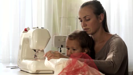 Joven-atractiva-madre-trabajando-en-la-máquina-de-coser-con-su-hija-poco-Linda