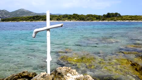 Christlichen-weißen-Holzkreuz-am-felsigen-Ufer-des-blauen-Meeres.-Küste-der-Insel-Hvar-und-Hafen-in-der-Altstadt-von-Hvar.