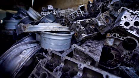 metal-parts-of-old-broken-automobiles-are-lying-in-heaps-of-scrap-metal-in-large-hangar,-old-humps-and-engines