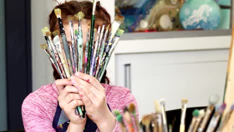 Cute-happy-girl-smiling-to-the-camera-holding-bunch-of-paintbrushes