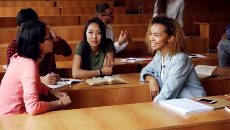 Las-mujeres-jóvenes-tienen-conversación-después-de-conferencias-en-el-colegio,-niñas-hablando-y-gesticulando-mientras-que-otros-estudiantes-están-charlando-en-el-fondo.-Concepto-de-joven-y-en-la-comunicación.